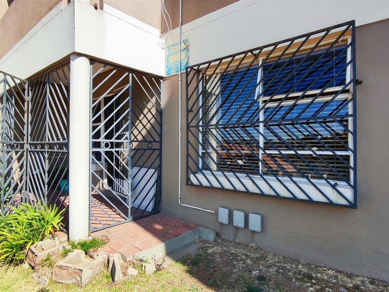 Front entrance of the townhouse featuring security gates and bars, concrete pillar, and paved access area with visible exterior wall wear.