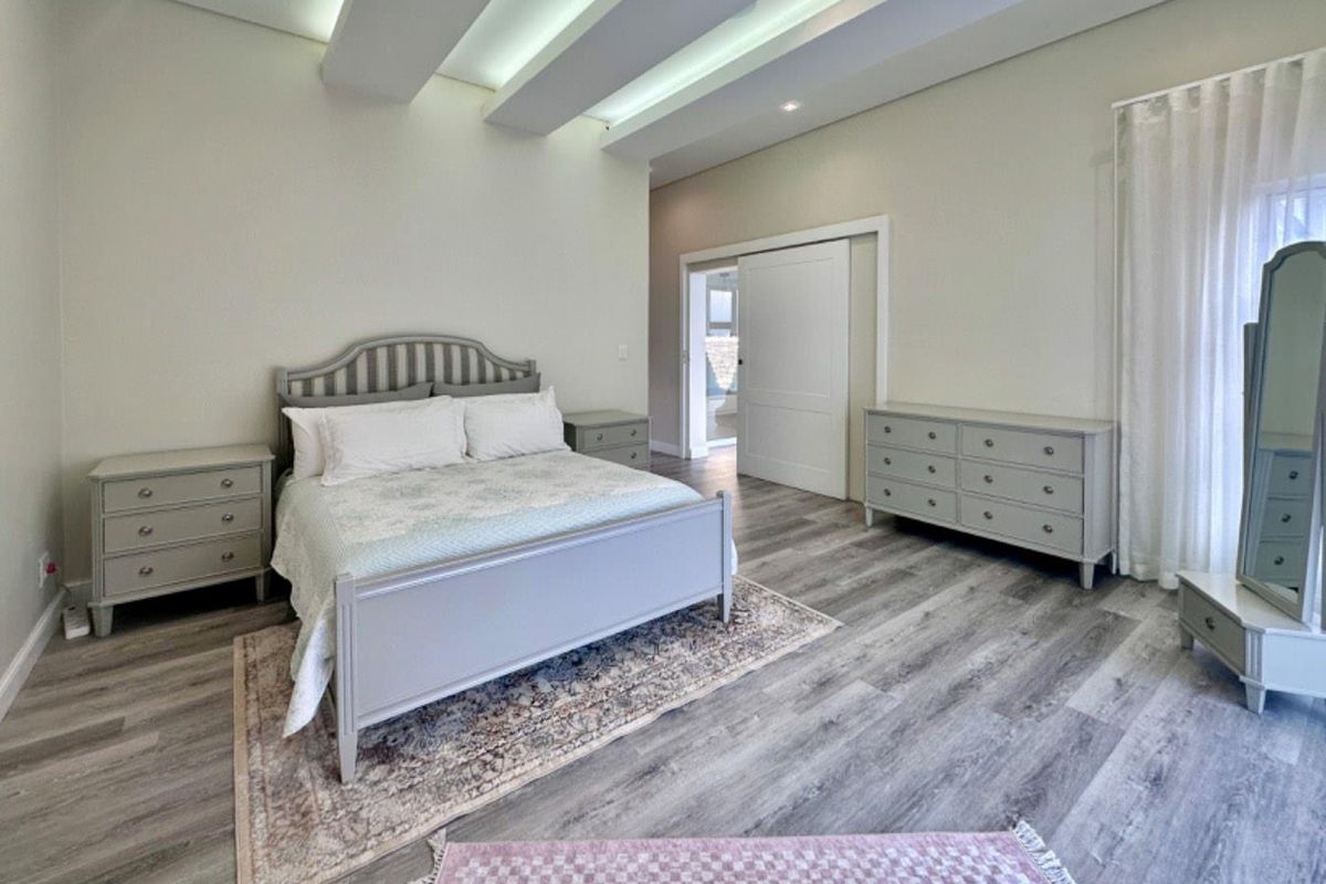 Spacious bedroom featuring modern laminate flooring, a distinctive coffered ceiling with recessed lighting, and a sliding door leading to an adjoining space.