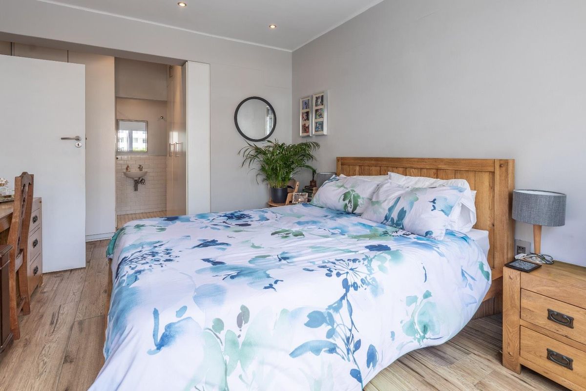 A well-maintained bedroom featuring wood-look flooring, recessed ceiling lighting, and an adjoining en-suite bathroom with tiled finishes.