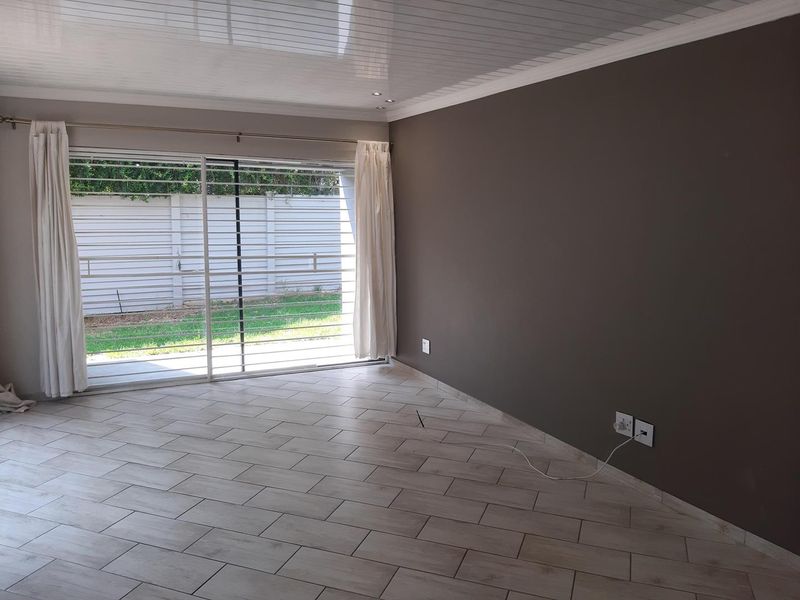 An empty living room featuring modern tiled flooring, a PVC ceiling with recessed lighting, and a large sliding glass door with security bars.