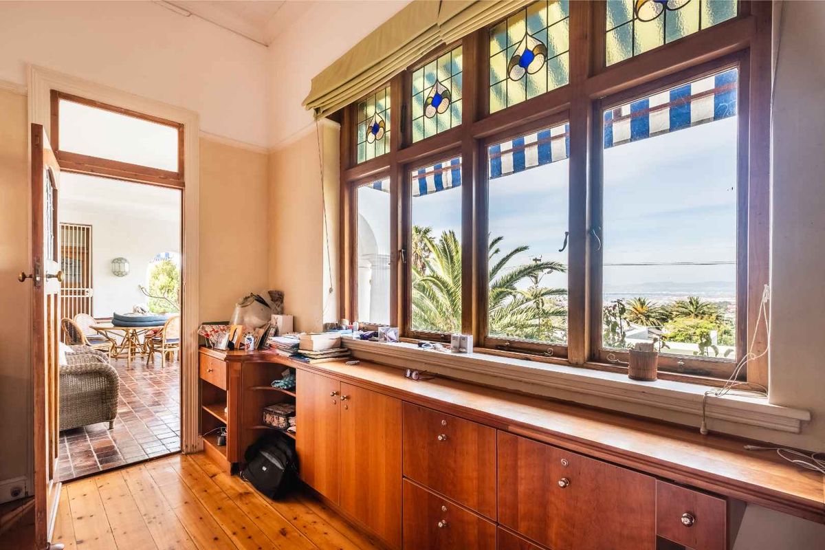 A sunlit living area featuring classic stained glass windows, polished timber flooring, and extensive built-in timber cabinetry with views of the surrounding landscape.