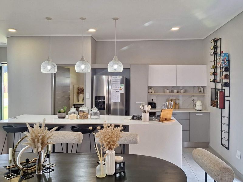 Modern open-plan kitchen featuring a central island, sleek cabinetry, stone countertops, and contemporary pendant lighting, seamlessly integrated with the dining area.