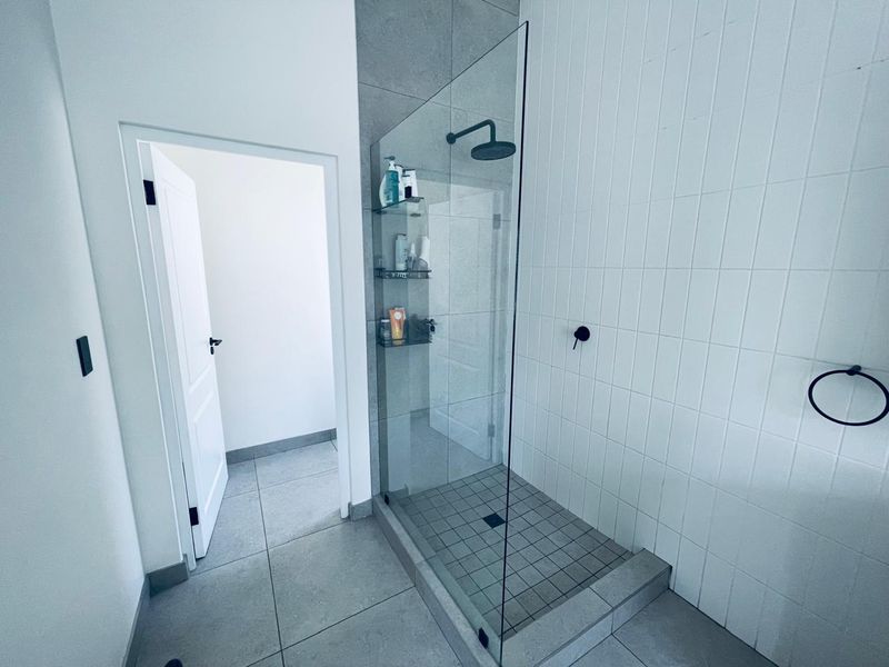 Modern bathroom featuring a spacious walk-in shower with a glass screen, contemporary matte black fixtures, and neutral floor-to-ceiling tiling.