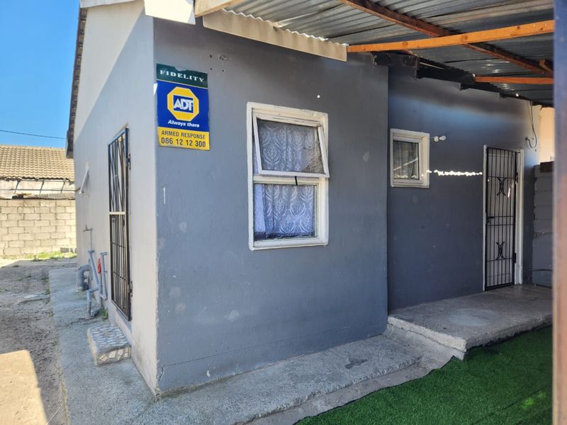 Rear exterior view of the property featuring a concrete patio, security gates, and a corrugated roof structure.