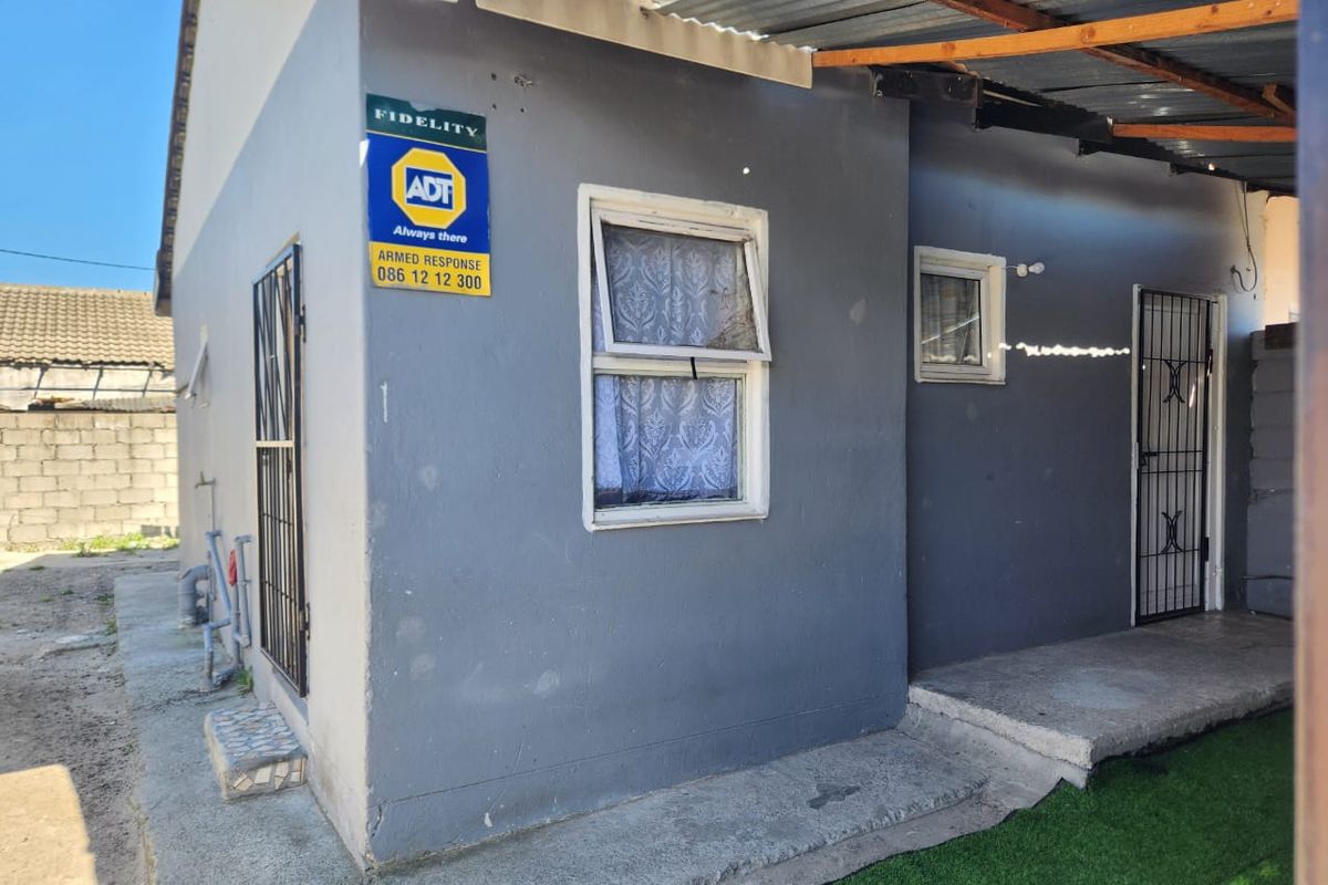Rear exterior view of the property featuring a concrete patio, security gates, and a corrugated roof structure.