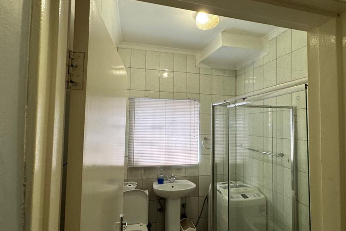 A functional bathroom featuring a pedestal basin, toilet, and a glass-enclosed shower with tiled walls and flooring.