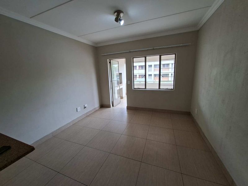 An empty living room featuring neutral tiled flooring, a ceiling light fixture, and access to an outdoor area through an aluminium door.