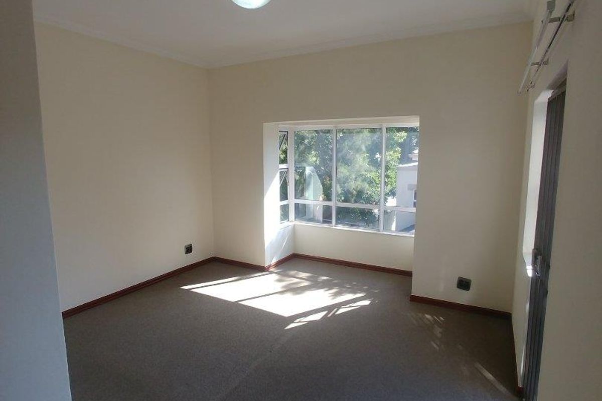 A bright, empty bedroom featuring neutral walls, carpeted flooring, and a large window providing natural light.