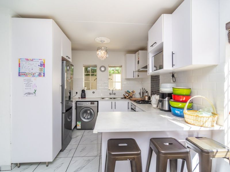 A functional kitchen featuring white cabinetry, subway tile backsplash, a breakfast counter, and modern marble-look floor tiles.