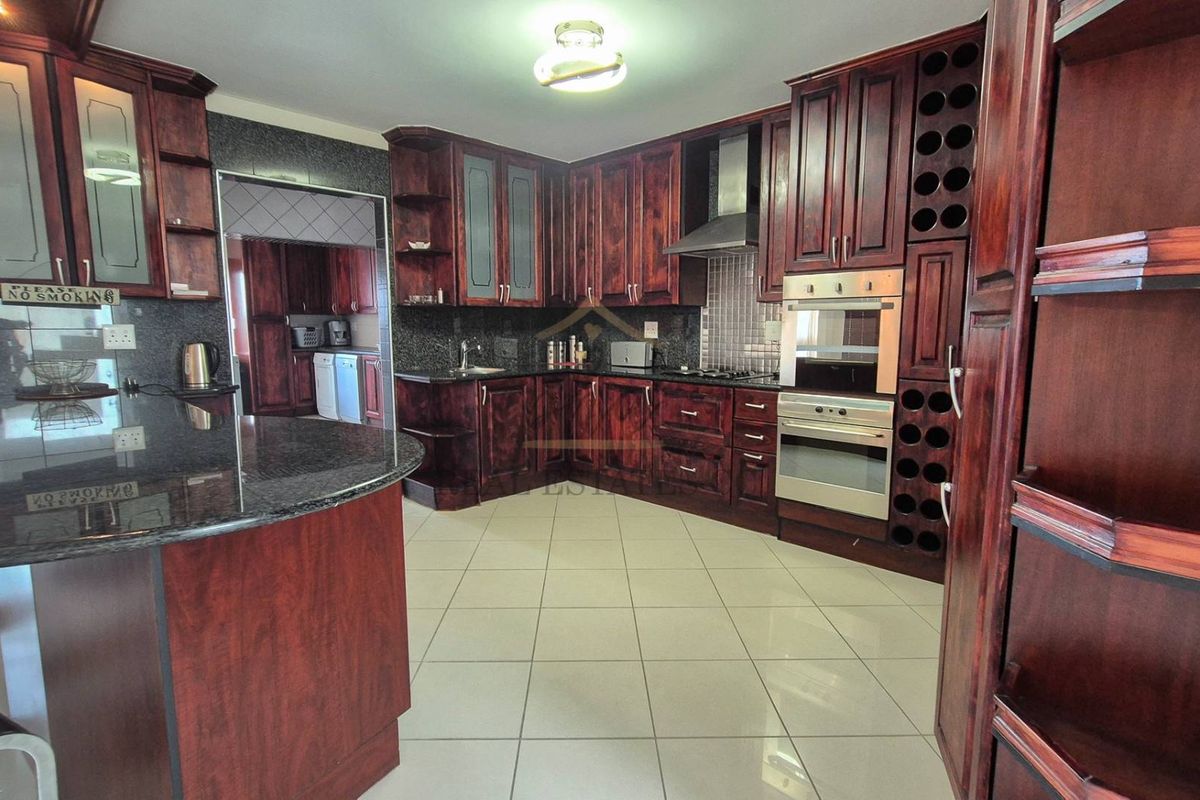 Spacious kitchen featuring dark wood cabinetry, granite countertops, built-in oven, extractor fan, and tiled flooring, with an adjacent scullery area.