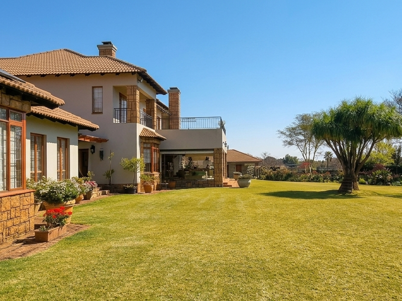 Spacious rear garden featuring a well-maintained lawn, mature trees, and a multi-level residence with stone accents, timber windows, and a covered patio area.