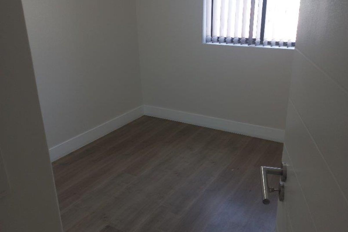 An empty bedroom featuring neutral walls, laminate flooring, and vertical window blinds, offering a clean and versatile space.