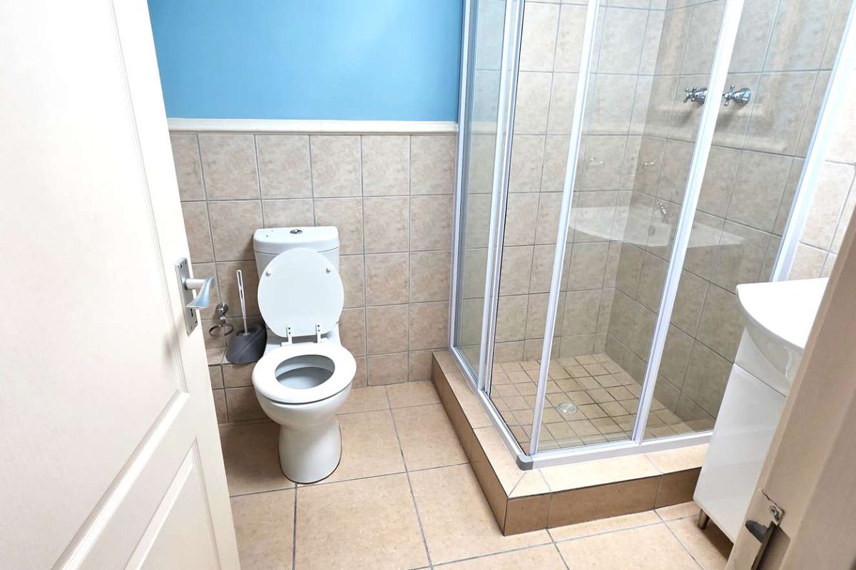 A functional bathroom featuring a tiled shower enclosure, a standard toilet, and a vanity unit with neutral wall finishes.
