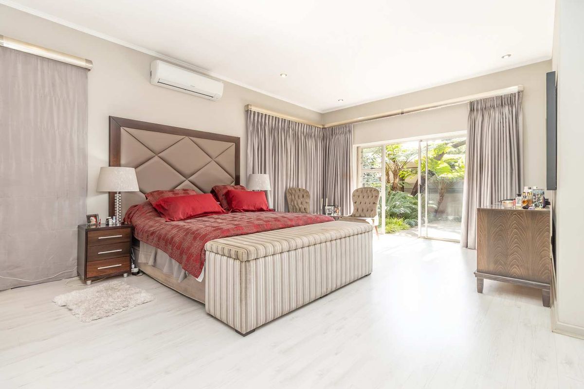 Spacious bedroom featuring light wood-look flooring, a wall-mounted air conditioning unit, and large sliding glass doors providing direct access to the garden.