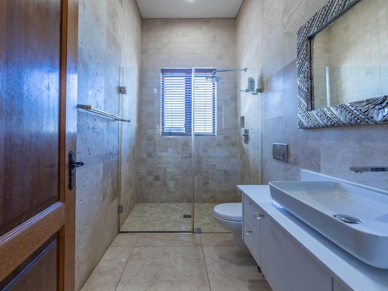 Modern bathroom featuring a walk-in shower with glass screen, wall-mounted toilet, and a sleek vanity unit with a vessel sink, finished in travertine tiling.