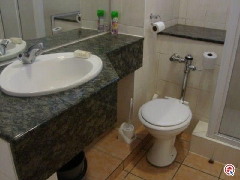 A functional bathroom featuring a granite vanity countertop with an undermount sink, tiled walls and flooring, and a separate shower enclosure.