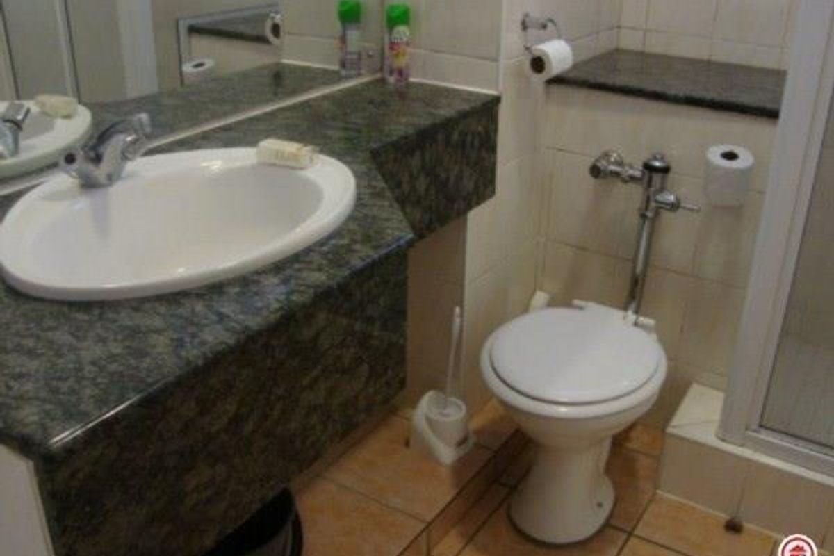 A functional bathroom featuring a granite vanity countertop with an undermount sink, tiled walls and flooring, and a separate shower enclosure.