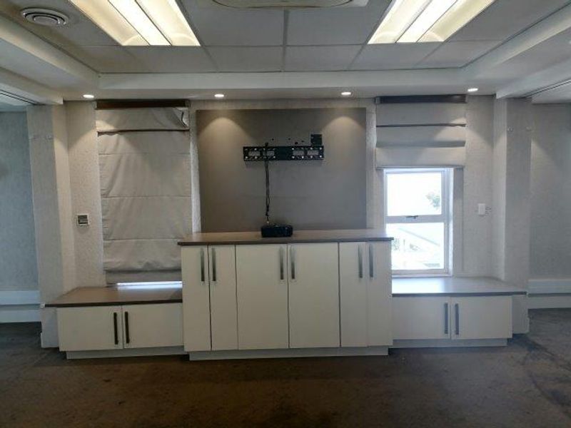 A professional office space featuring built-in storage cabinetry, recessed ceiling lighting, and roman blinds, providing a functional and organized work environment.