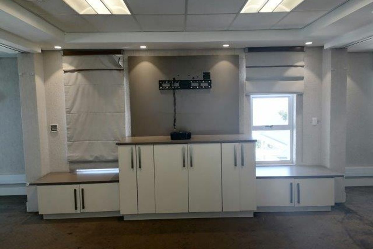 A professional office space featuring built-in storage cabinetry, recessed ceiling lighting, and roman blinds, providing a functional and organized work environment.
