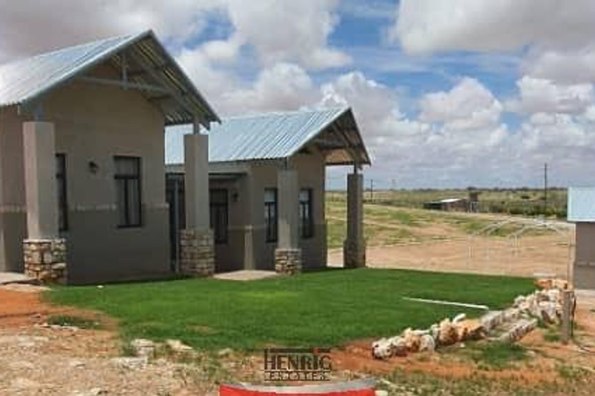 Exterior view of a modern guest house featuring corrugated metal roofing, stone-clad pillars, and a well-maintained lawn area.