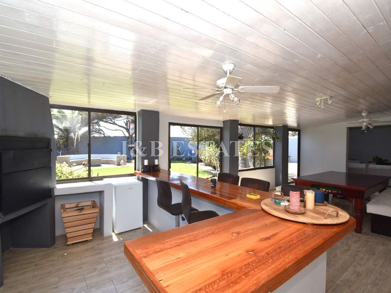Spacious covered patio featuring a built-in braai, wooden bar counter, and large windows overlooking the garden, ideal for outdoor entertaining.