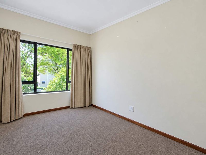 A bright, empty bedroom featuring neutral carpet flooring, large aluminium-framed windows, and classic coving, providing a clean canvas for personalization.