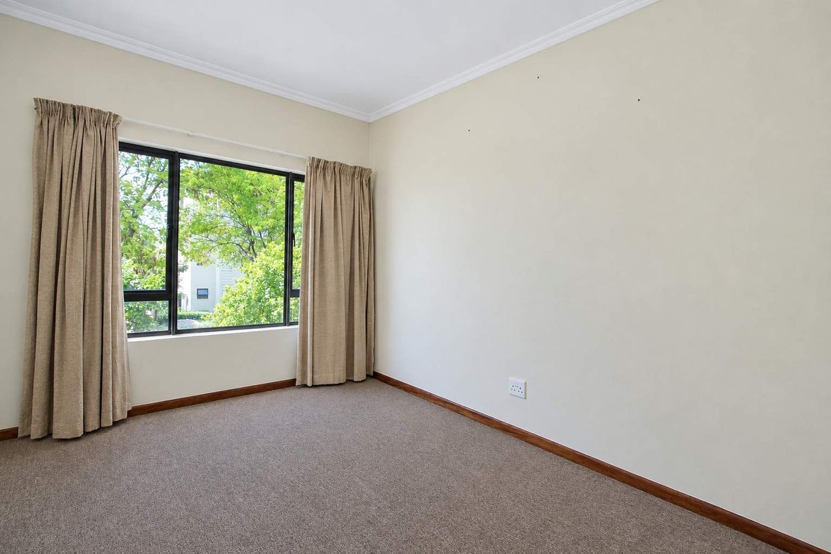 A bright, empty bedroom featuring neutral carpet flooring, large aluminium-framed windows, and classic coving, providing a clean canvas for personalization.