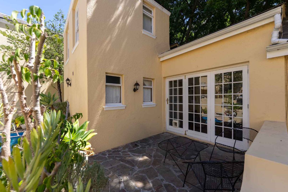 A rear patio area featuring stone paving, white French doors, and exterior wall-mounted lighting, adjacent to a multi-level townhouse structure.