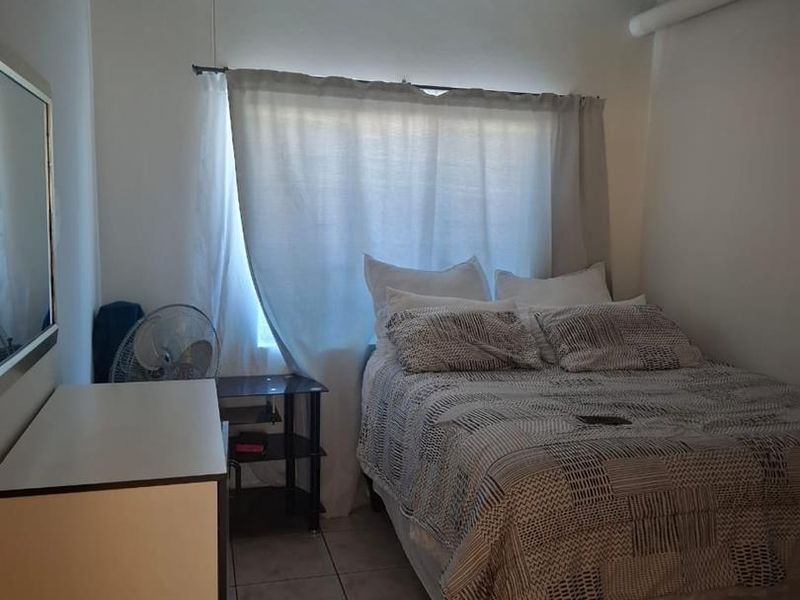 A compact bedroom featuring tiled flooring and a window with a curtain rod, providing a functional and neutral living space.