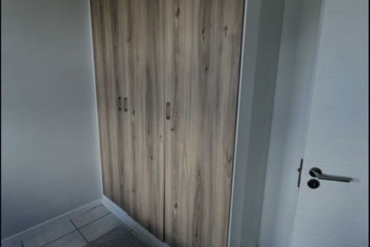 A bedroom featuring a modern wood-finish built-in wardrobe, neutral wall paint, and tiled flooring.