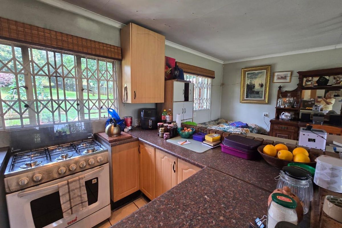 A functional kitchen featuring wooden cabinetry, a gas stove, and a breakfast counter, overlooking the garden through security-barred windows.