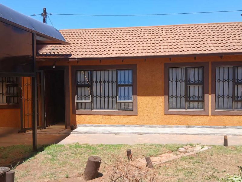 Rear view of the house featuring a tiled roof, textured exterior walls, security bars on windows, and a paved patio area leading to the garden.