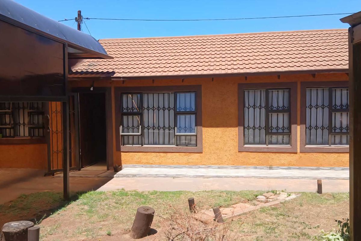 Rear view of the house featuring a tiled roof, textured exterior walls, security bars on windows, and a paved patio area leading to the garden.