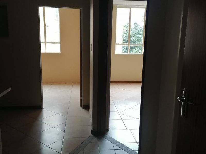 A dimly lit hallway with tiled flooring connecting multiple rooms, featuring standard internal doors and window frames.