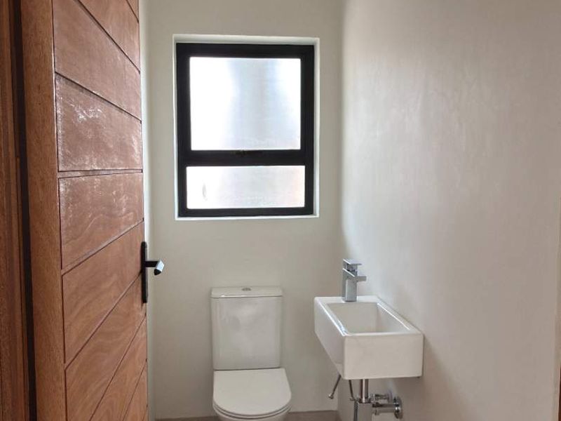A modern, minimalist guest bathroom featuring a wall-mounted basin, toilet, and timber door, finished with clean neutral tones.