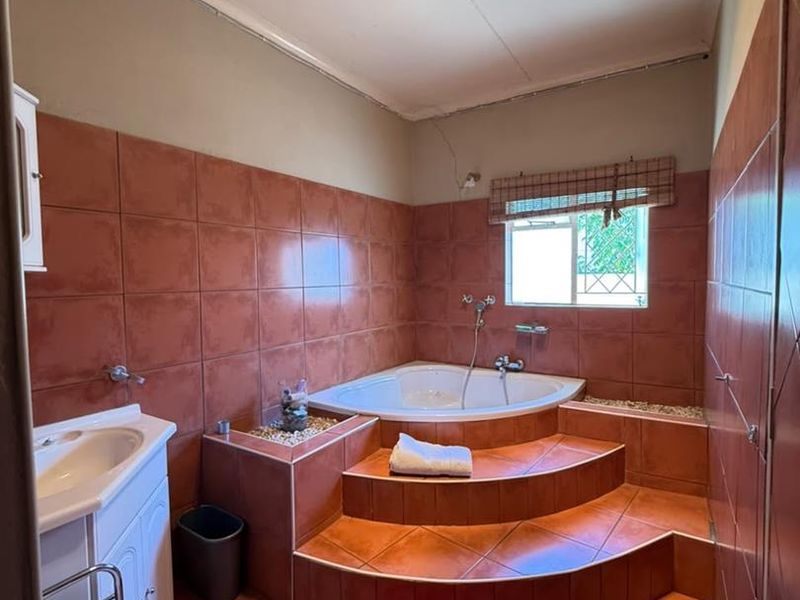 Bathroom featuring a raised corner bathtub with tiled steps, ceramic wall and floor tiling, and a vanity basin.