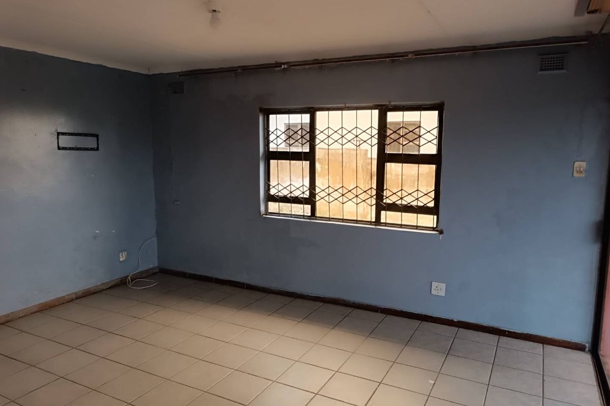 An empty living room featuring tiled flooring, blue painted walls, and a window fitted with security bars.
