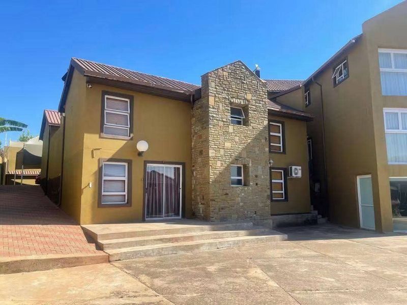 Rear exterior view of a multi-story house featuring stone cladding, a concrete patio area, and paved driveway access.