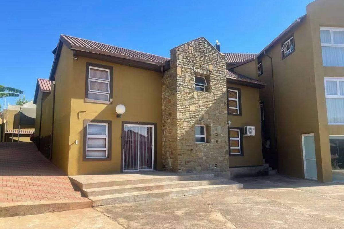 Rear exterior view of a multi-story house featuring stone cladding, a concrete patio area, and paved driveway access.