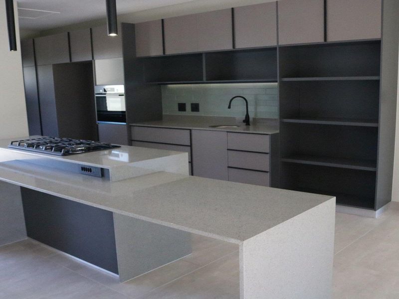 Modern kitchen featuring sleek grey cabinetry, stone countertops, a central island with a gas hob, and integrated appliances in a clean, contemporary design.