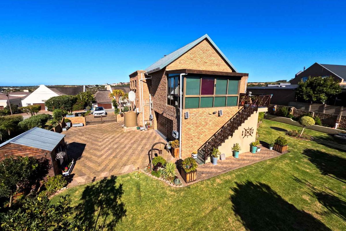Aerial view of a two-story brick house featuring a paved driveway, external staircase, balcony, and a well-maintained garden with a small storage shed.