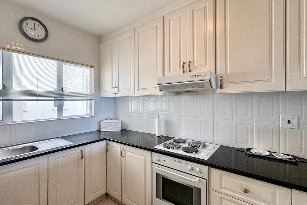 A functional kitchen featuring white cabinetry, black granite countertops, a tiled backsplash, and integrated appliances including an oven and hob.