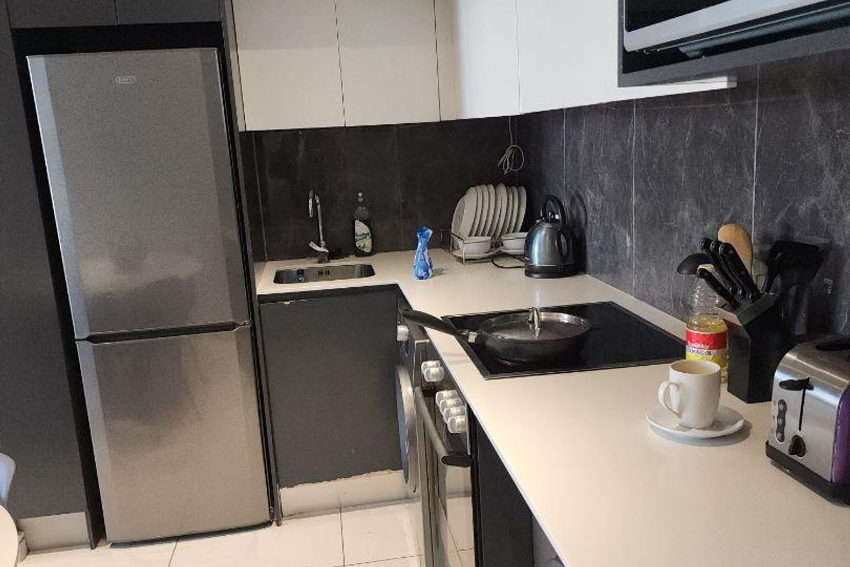 Modern kitchen featuring sleek dark and white cabinetry, stone-look countertops, integrated sink, and built-in appliances including a hob and microwave.
