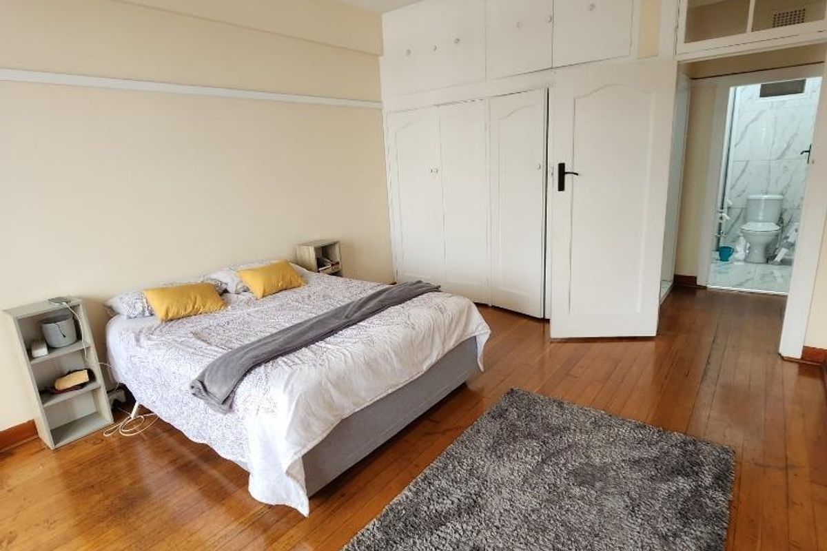 Spacious bedroom featuring polished hardwood flooring, extensive built-in cabinetry with overhead storage, and direct access to an en-suite bathroom.