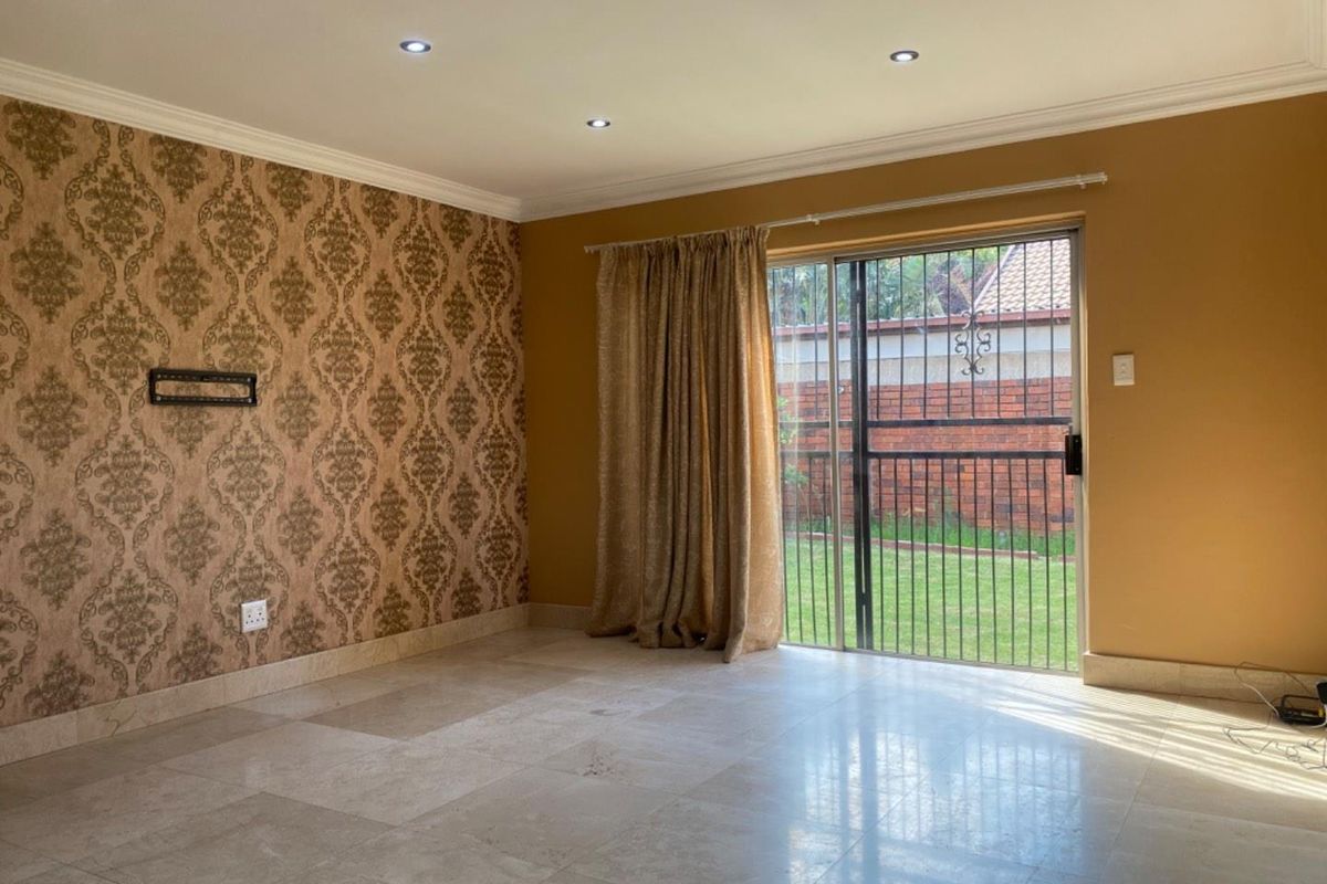 Spacious living room featuring tiled flooring, decorative wallpaper accent wall, and sliding glass door with security gate leading to the rear garden.