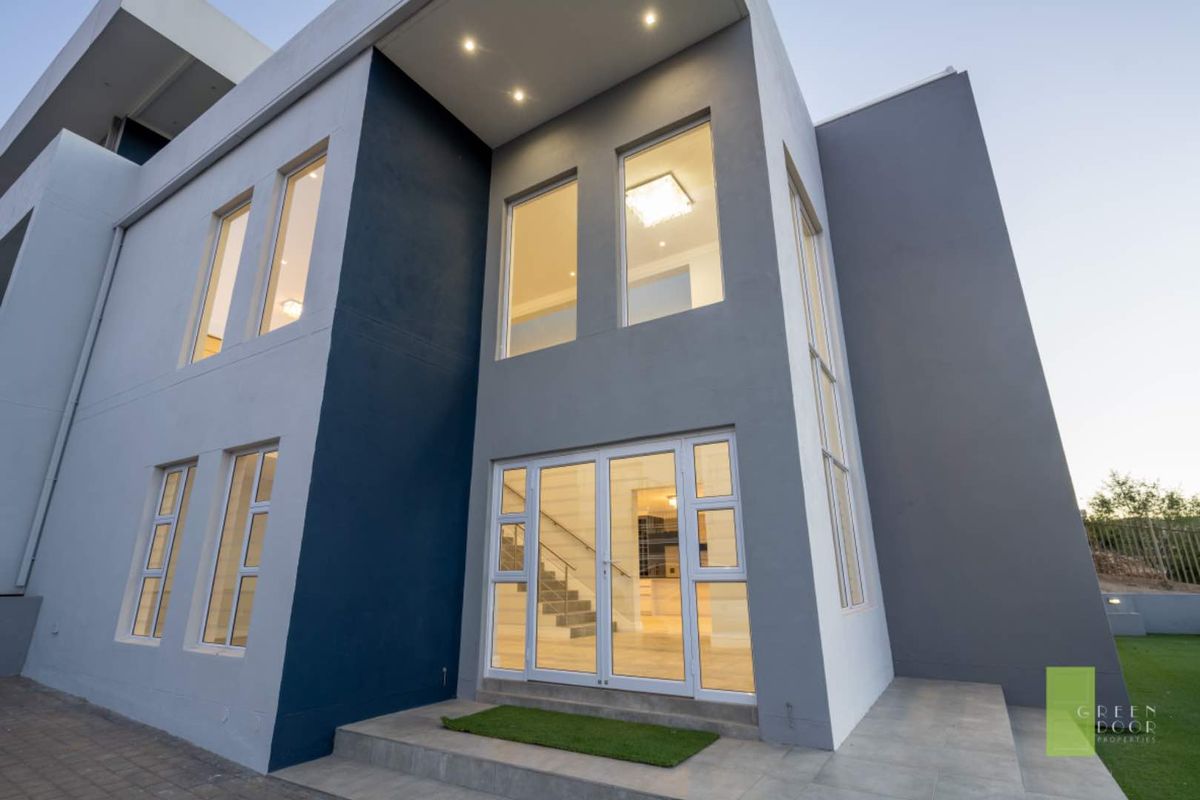 Modern double-storey exterior facade featuring contemporary grey and navy finishes, large glass windows, and a welcoming entrance with tiled steps.