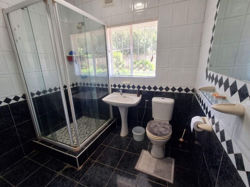 A functional bathroom featuring a glass shower enclosure, pedestal basin, and toilet, finished with black and white decorative wall and floor tiling.