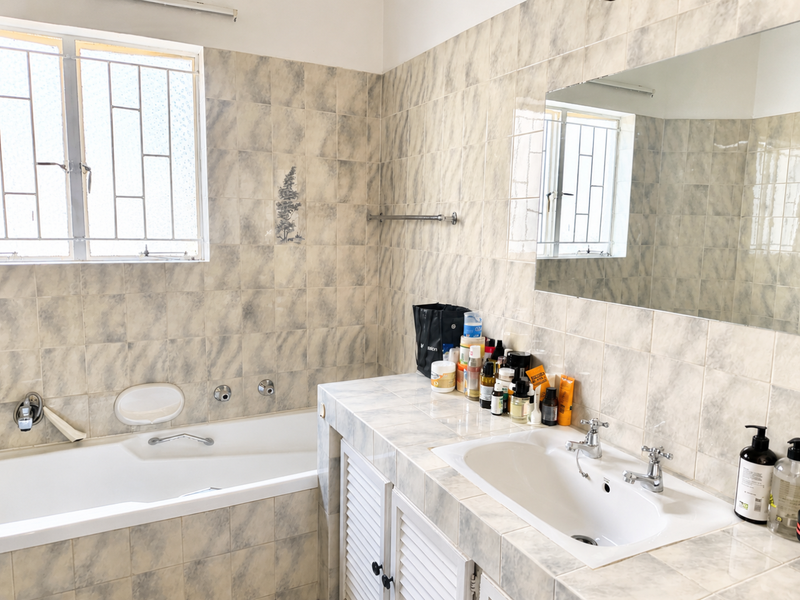 A functional bathroom featuring a built-in bathtub, tiled vanity with inset basin, and wall-mounted mirror, finished with neutral wall tiles.