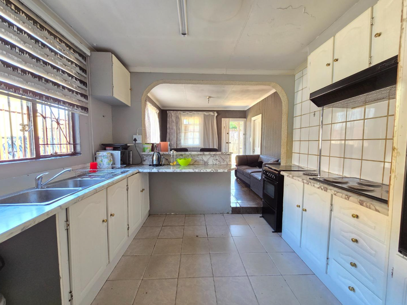 Open-plan kitchen featuring white cabinetry, laminate countertops, and a double basin sink, flowing into an adjacent living area through a decorative archway.
