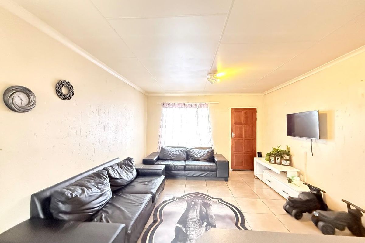 A living room featuring tiled flooring and a wooden entrance door, providing a functional and open living space.